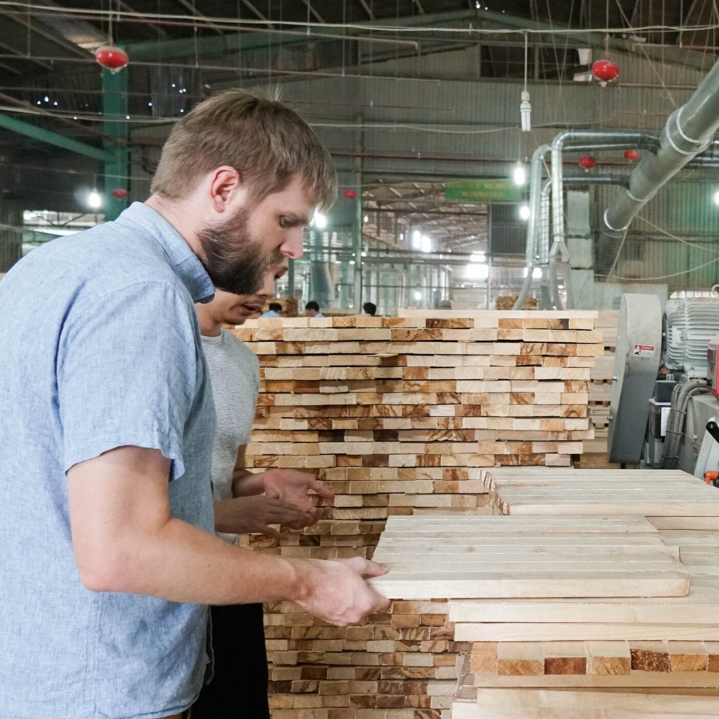 Two men inspecting a stack of wooden planks inside a woodworking factory.